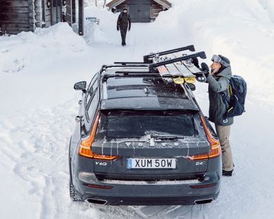 A woman stands in the snow and unloads her skis from a vehicle with a ski rack.
