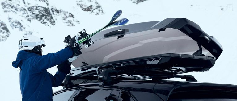A close-up of a person loading their skis into a Thule ski box.