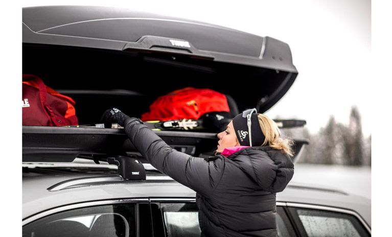 A close-up of a woman grabbing her skis from an open roof box with Thule duffels inside.